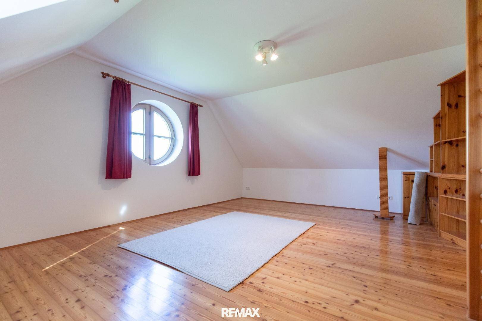 Geräumiges Dachzimmer mit Holzboden und runden Fenstern, vielseitig nutzbar.