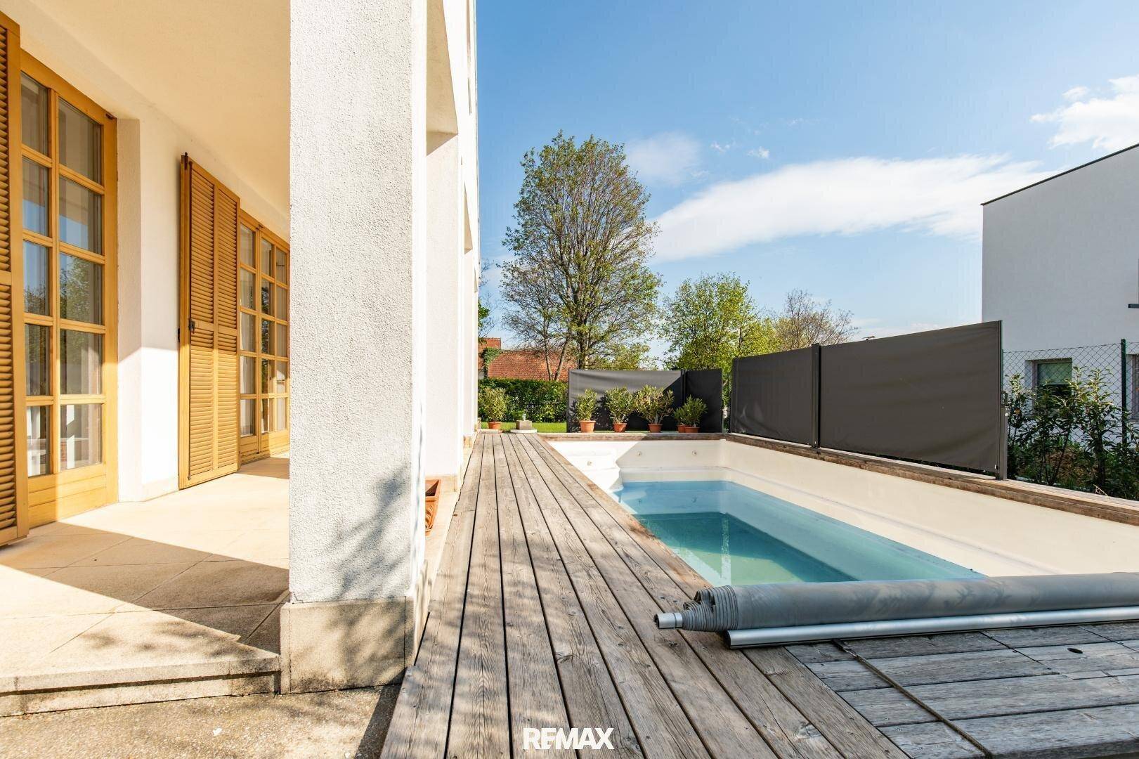 Holzdeck und eingelassener Pool neben der Hausfassade unter blauem Himmel.