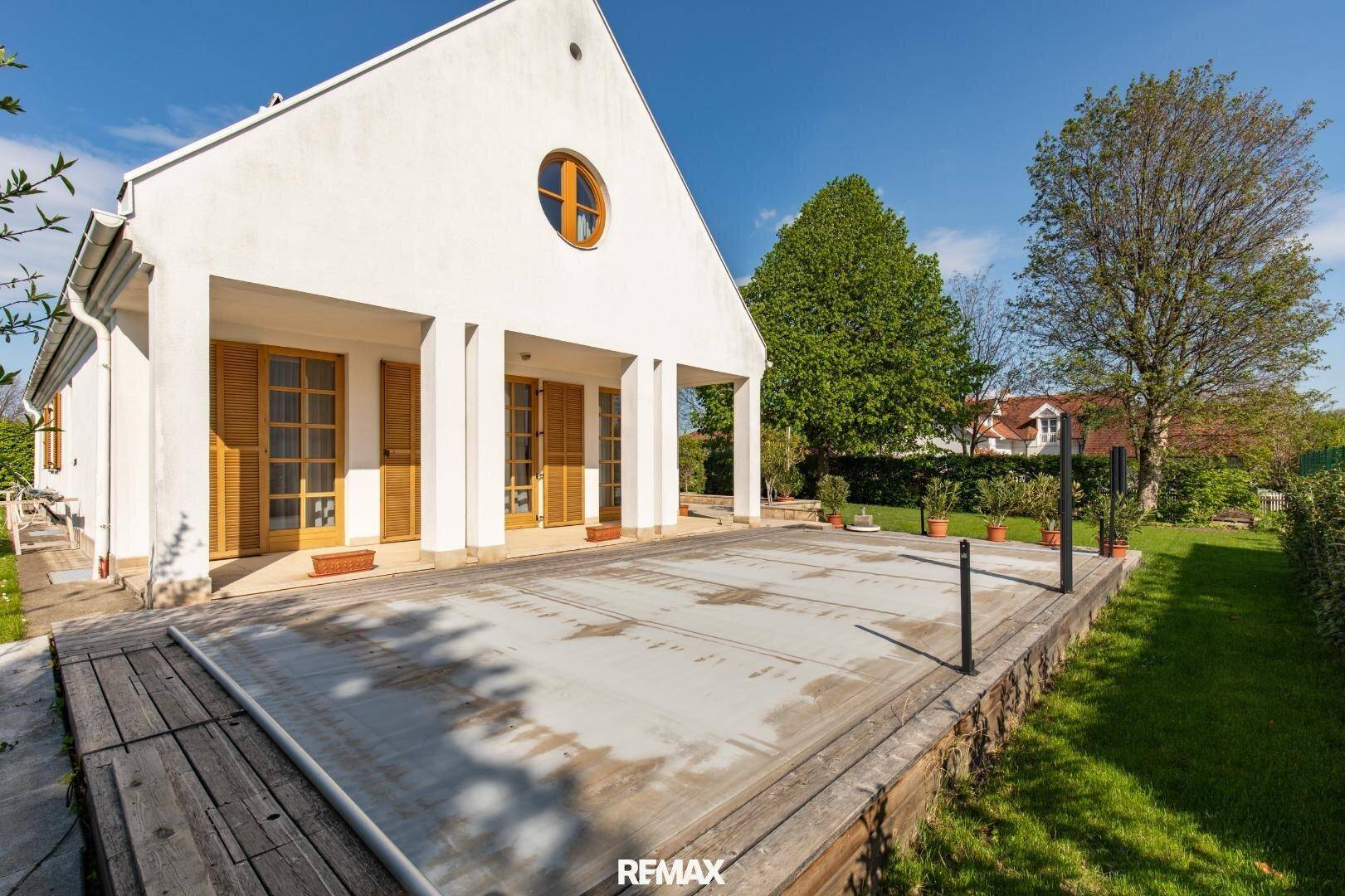 Außenansicht des Hauses mit abgedecktem Pool und Holzdeck im grünen Garten.