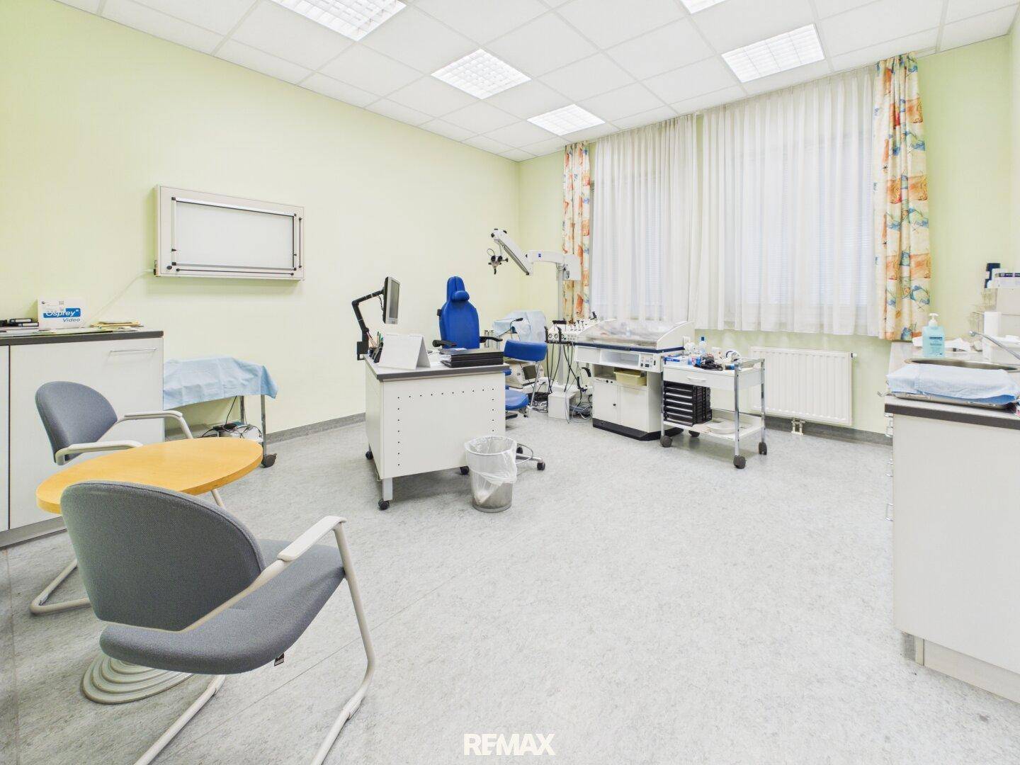 Behandlungszimmer mit medizinischer Ausstattung, Schreibtisch und hellgrünen Wänden.