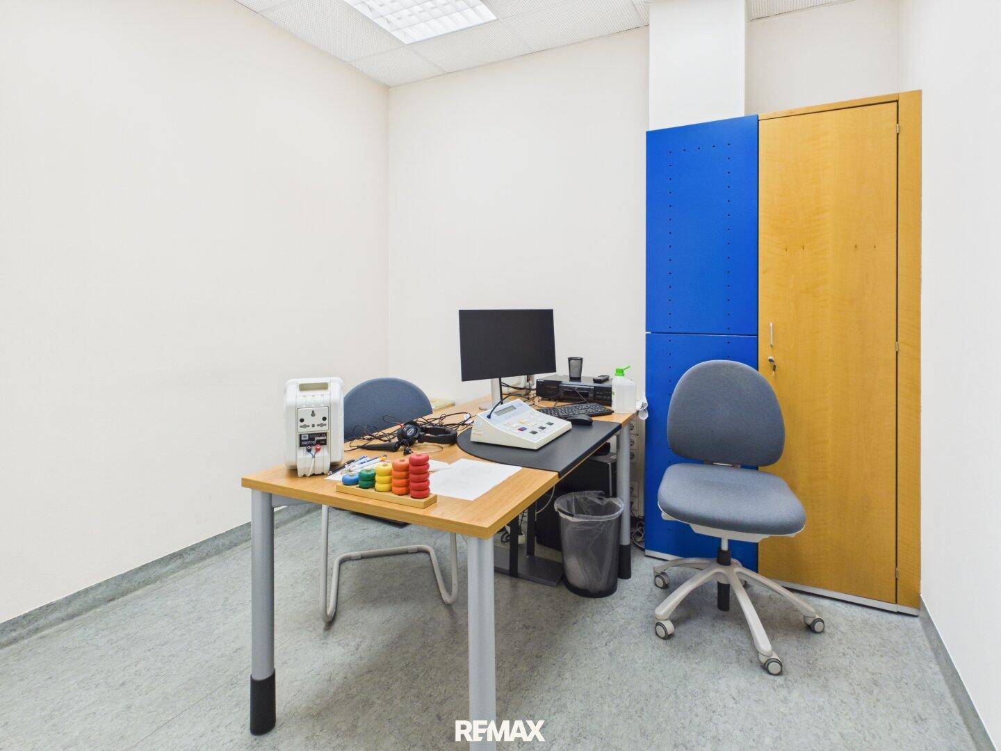 Kleines Büro oder Sprechzimmer mit Schreibtisch, Stuhl und blauen Einbauschränken.
