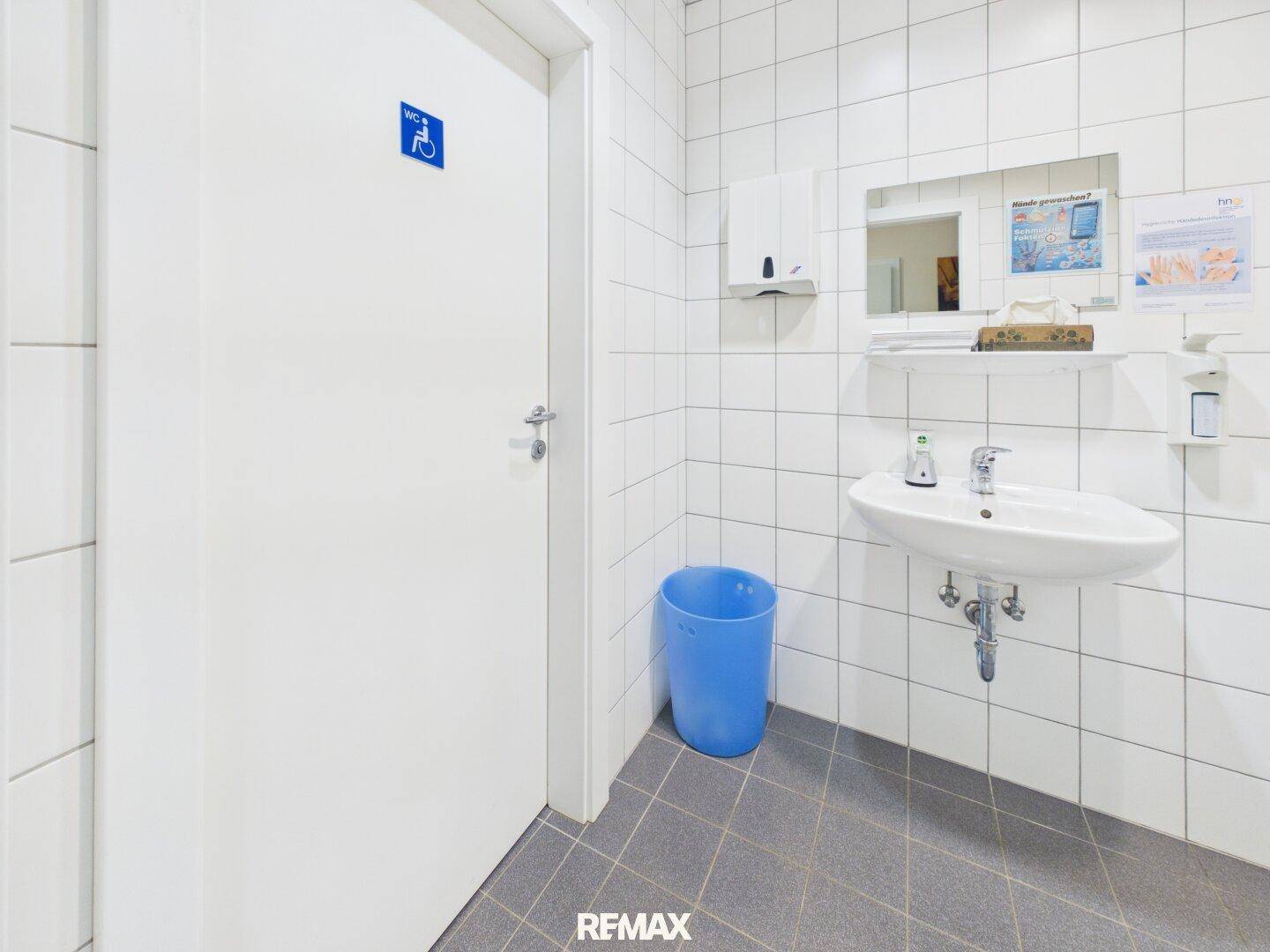 Barrierefreies WC mit Waschbecken, Spiegel und weißen Wandfliesen für optimale Hygiene.