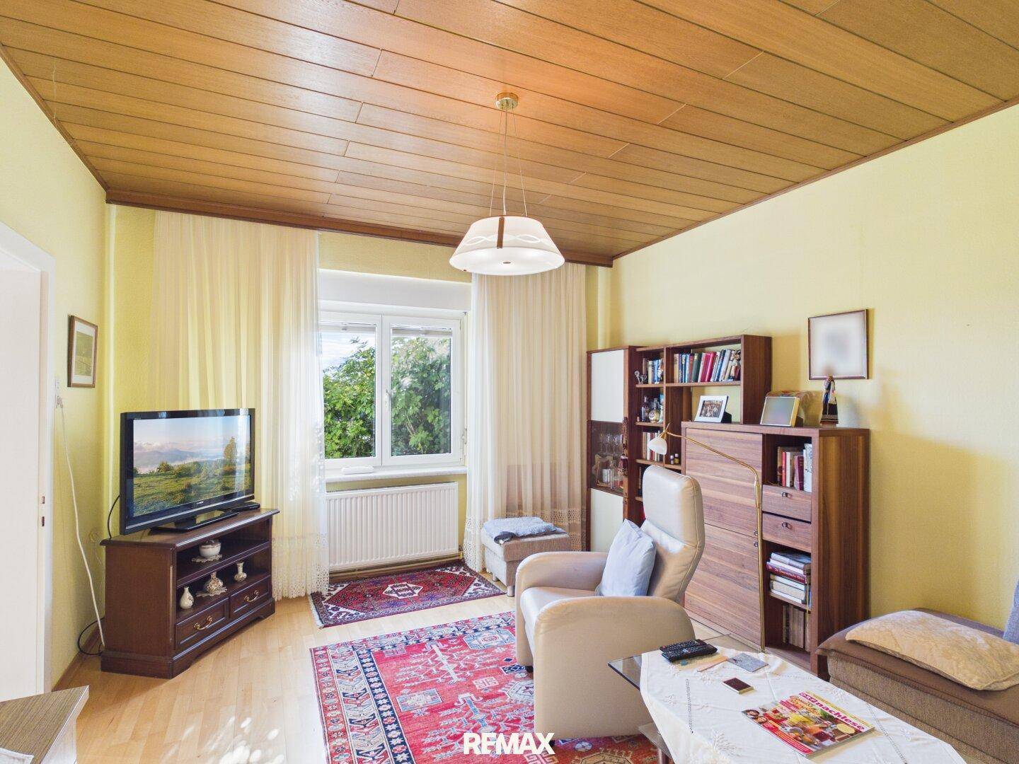 Gemütliches Wohnzimmer mit Holzdecke, Parkettboden und Blick in den Garten.