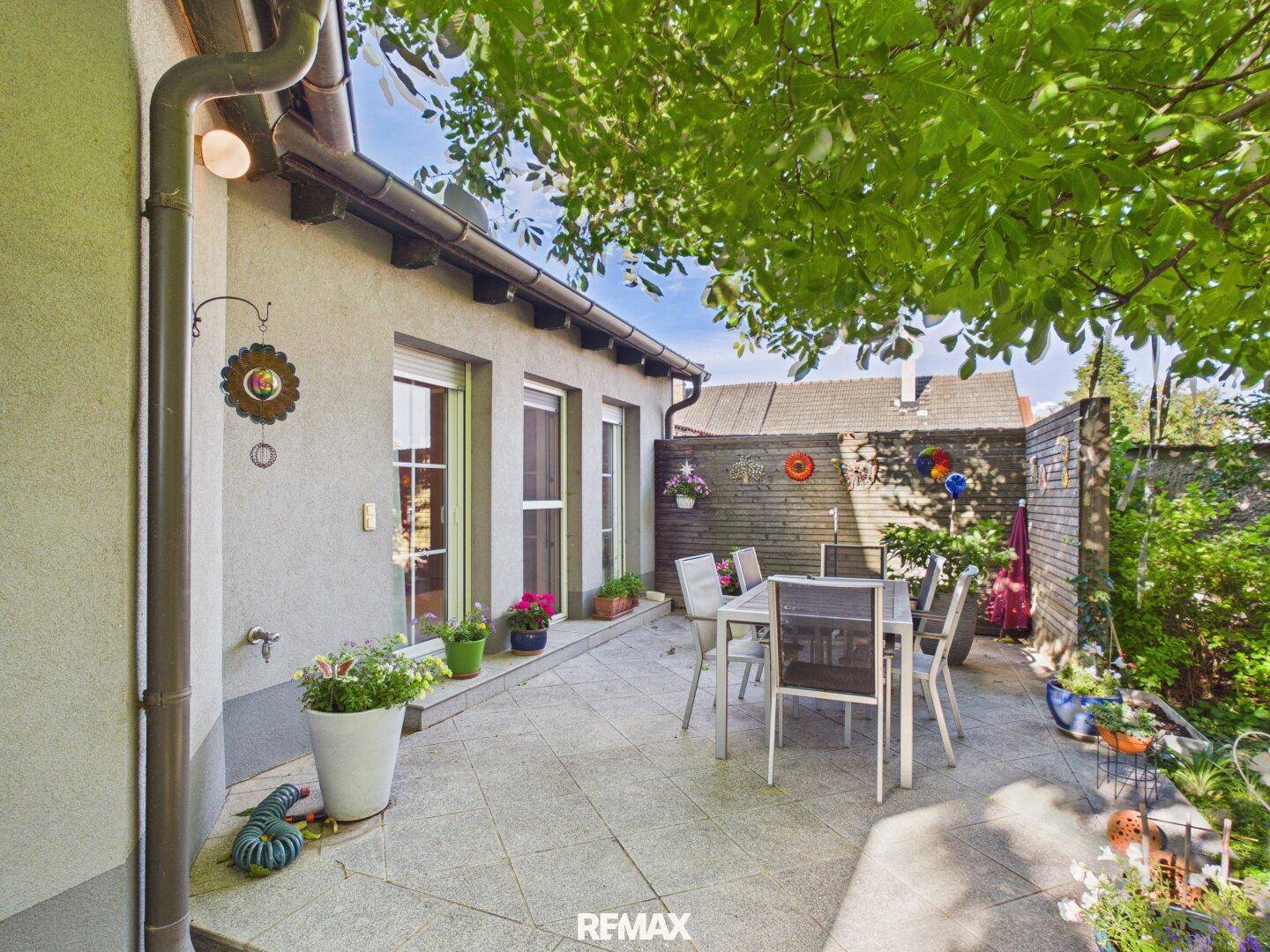 Geräumige Terrasse mit Fliesenboden und Gartenmöbeln, umgeben von viel Grün.