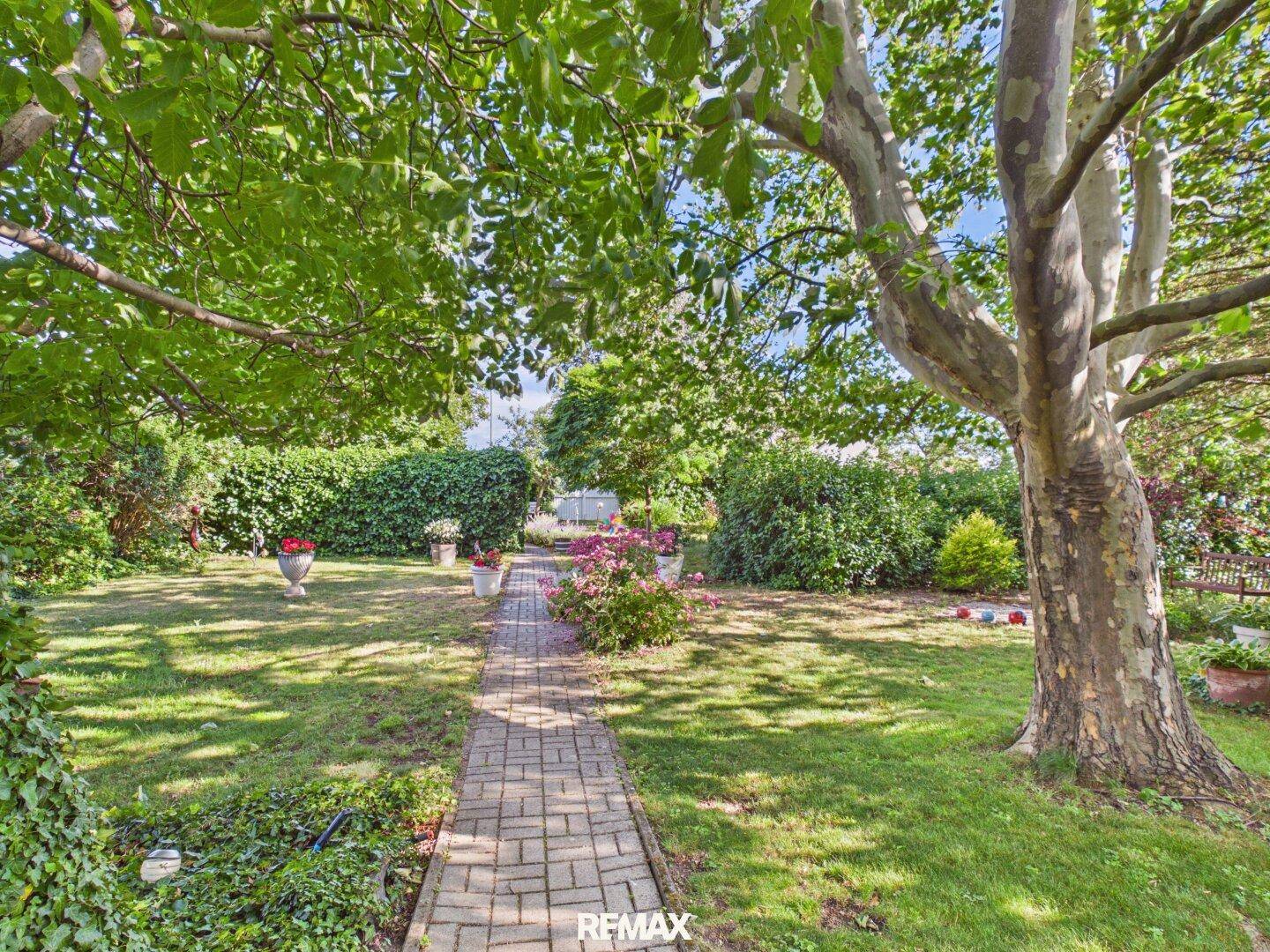 Großer, gepflegter Garten mit Rasenfläche, Bäumen und einem Steinweg.