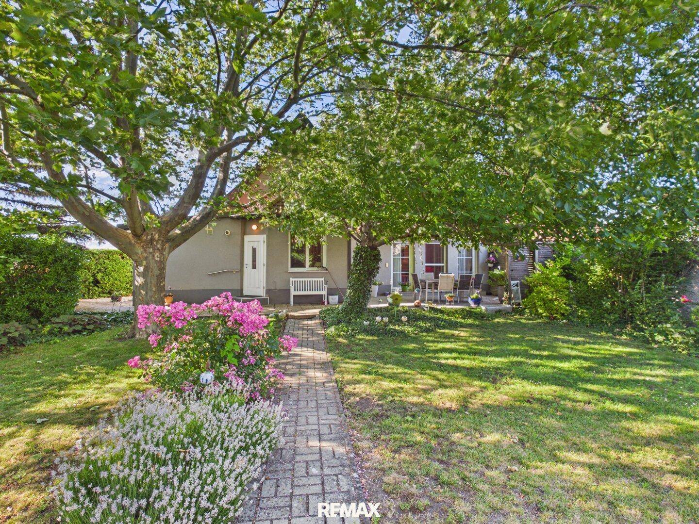 Das Haus ist eingebettet in einen weitläufigen Garten mit altem Baumbestand und Blumenbeeten.