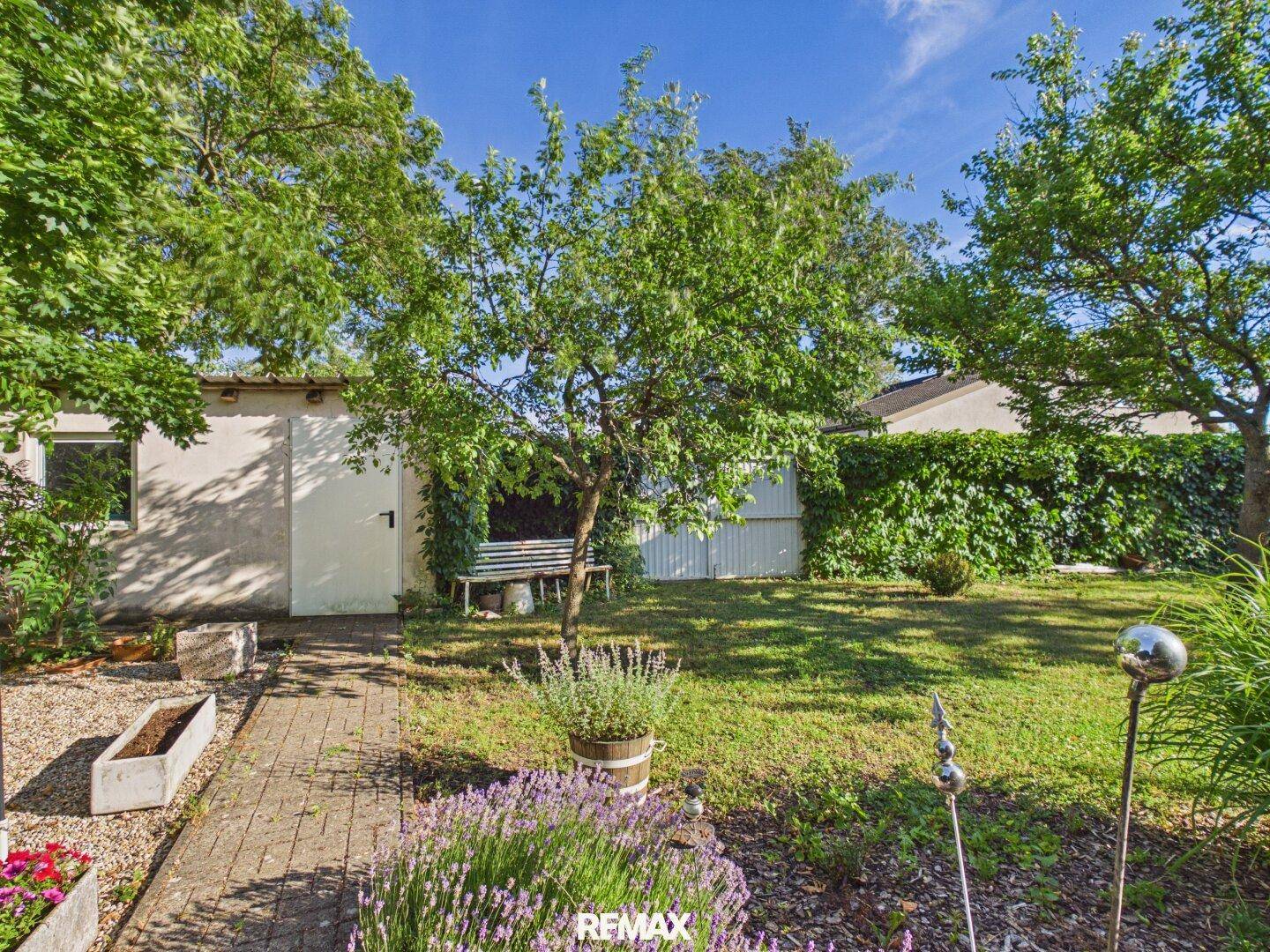 Gartenbereich mit Rasen, Bäumen und einem Gartenhaus im Hintergrund.
