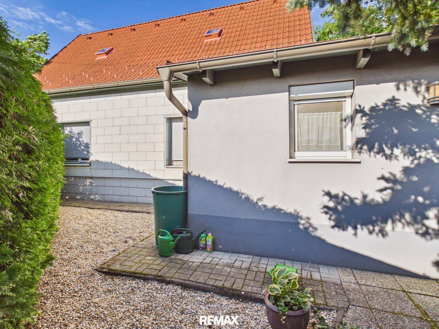 Seitenansicht des Hauses mit Kiesfläche und einem Mülleimer.