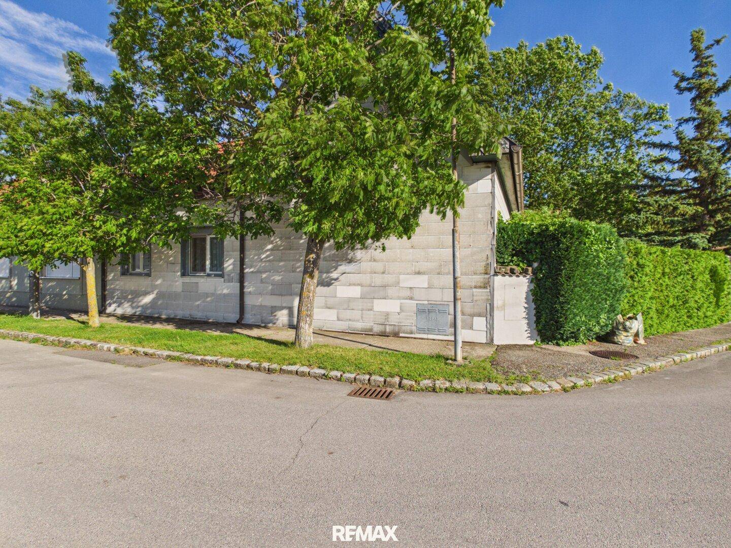 Eckansicht des Hauses von der Straße aus, umgeben von Bäumen und Hecken.