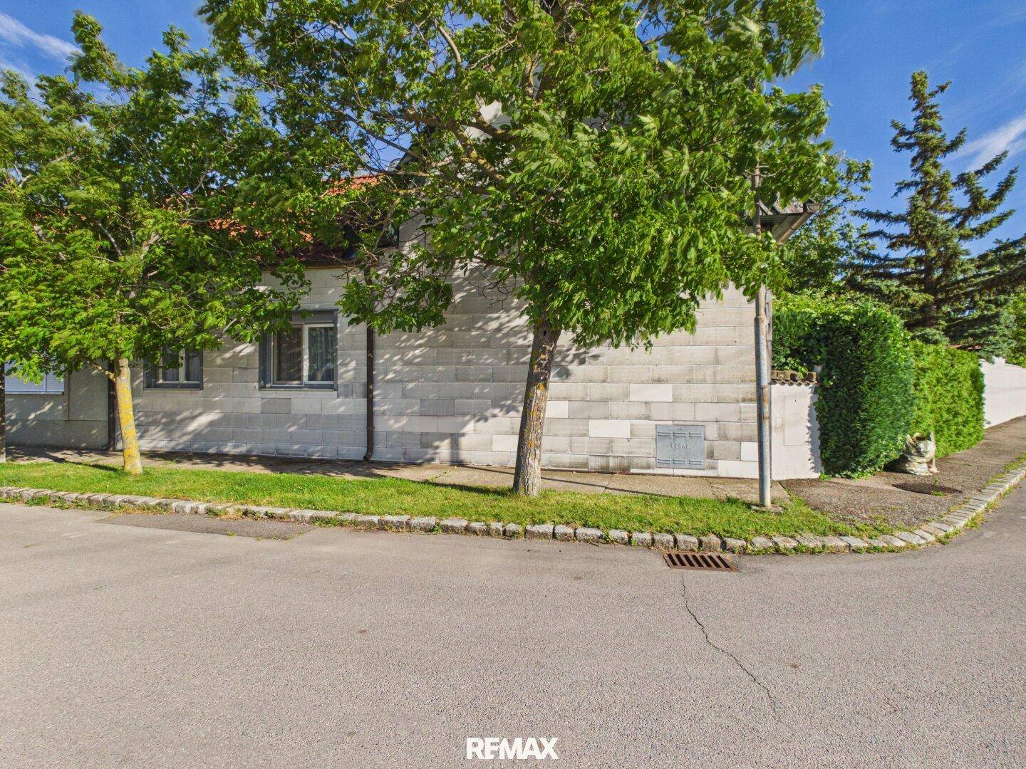 Das Haus von der Straßenseite aus gesehen, mit Bäumen und einer Hecke.