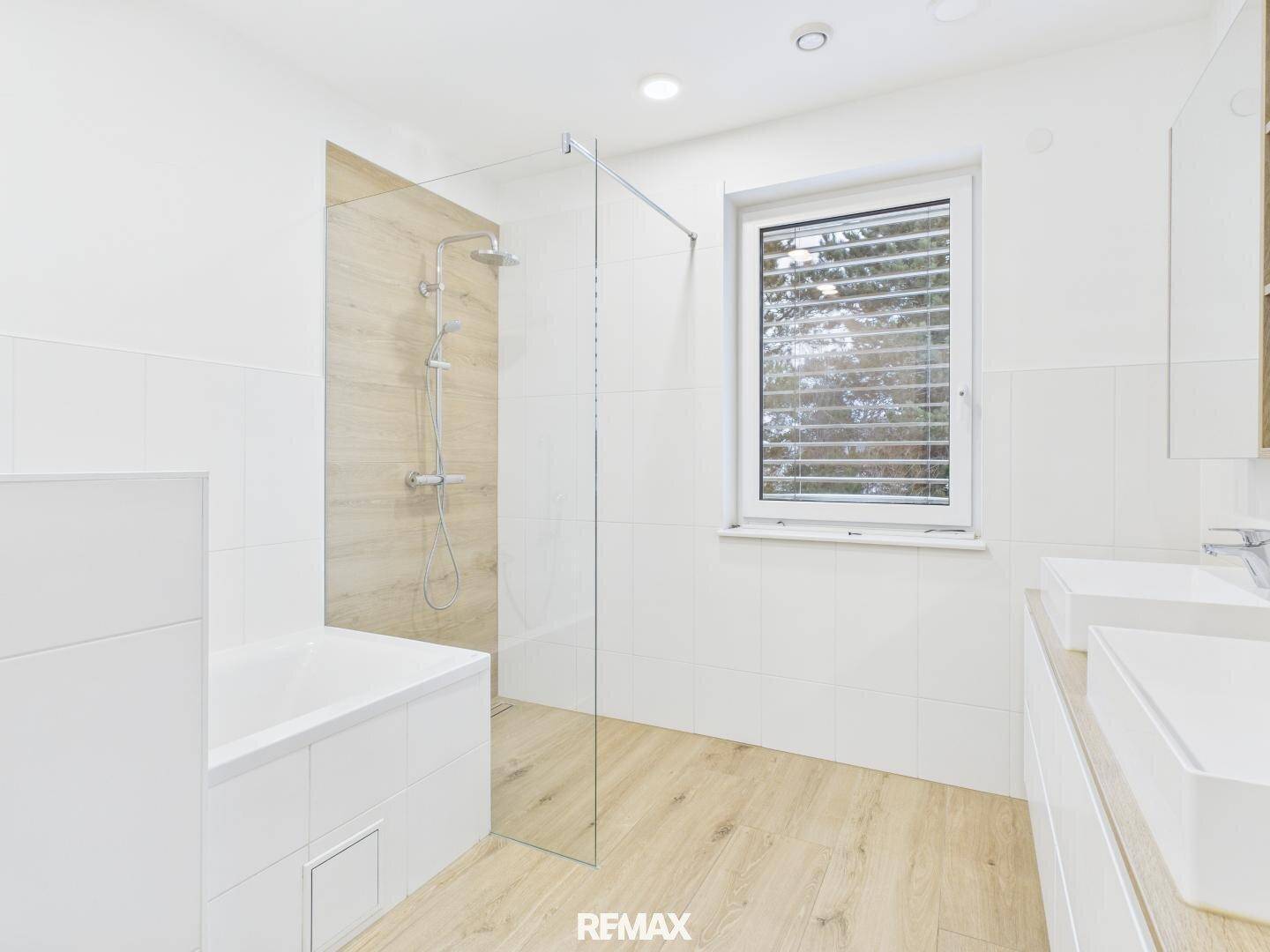 Helles Badezimmer mit Badewanne, begehbarer Dusche und Doppelwaschbecken.