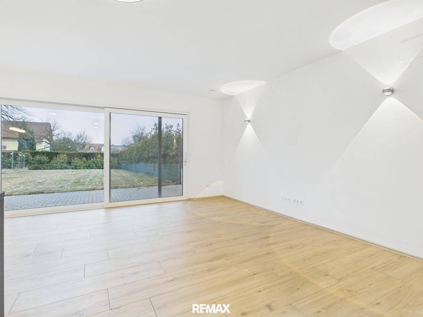 Helles, leeres Wohnzimmer mit großen Schiebetüren zum Garten und modernem Laminatboden.