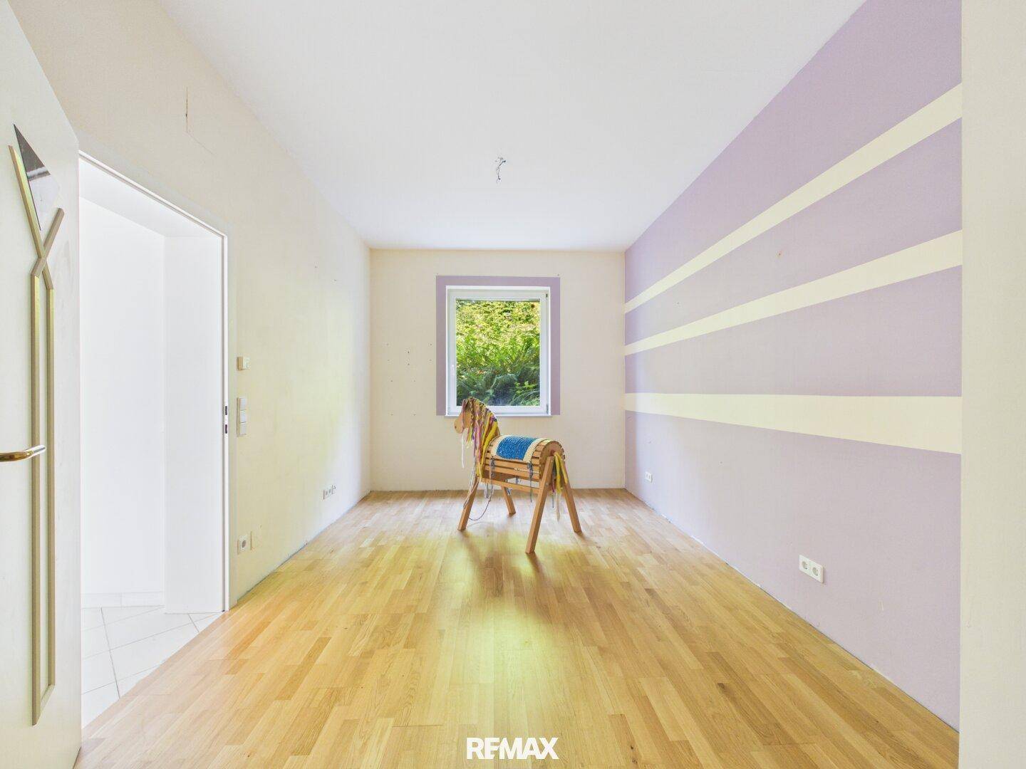 Helles Schlafzimmer mit Holzboden, farbiger Akzentwand und Fenster zum Garten.