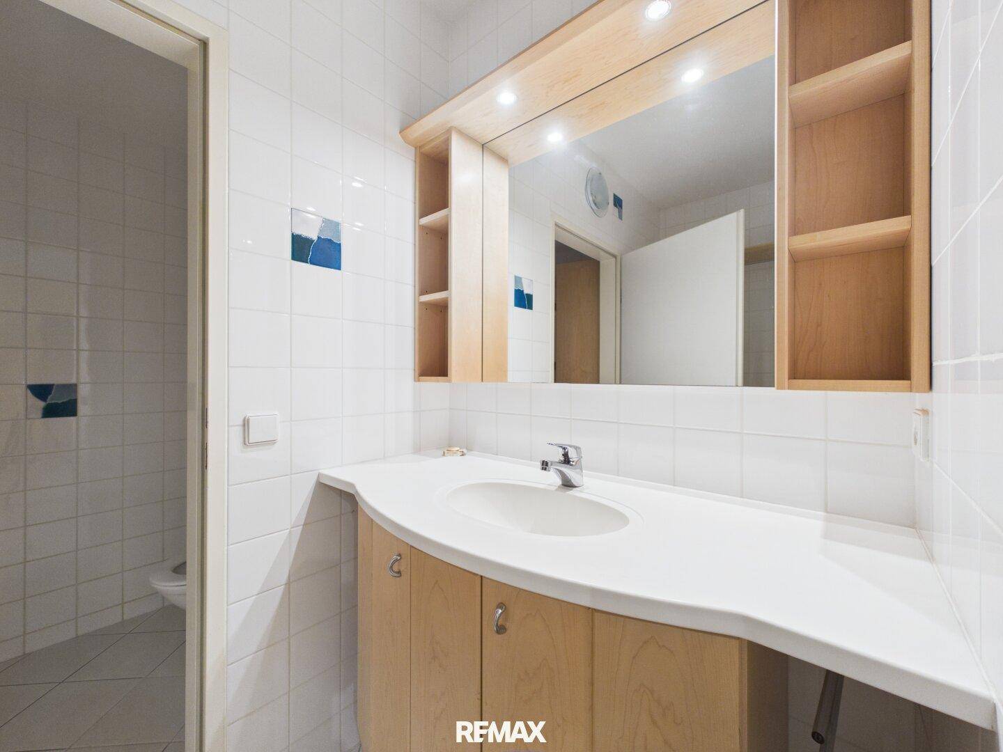 Badezimmer mit Einzelwaschbecken, Spiegelschrank und weiß gefliesten Wänden.