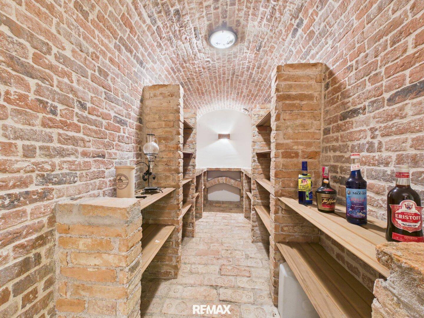 Historischer Weinkeller mit Ziegelgewölbe und Holzregalen für Flaschenlagerung, ideal für Weinliebhaber.