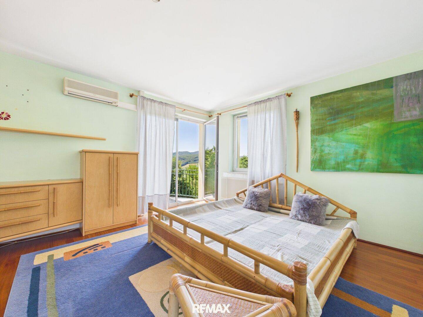 Schlafzimmer mit Balkonzugang, Holzboden und Blick auf die umliegende Landschaft.