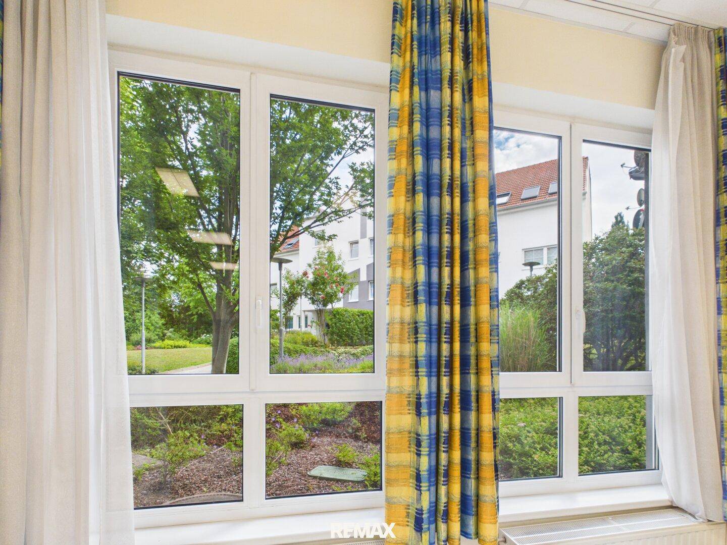 Große Fenster mit Blick ins Grüne und auf umliegende Gebäude, bieten viel Tageslicht und eine angenehme Aussicht.