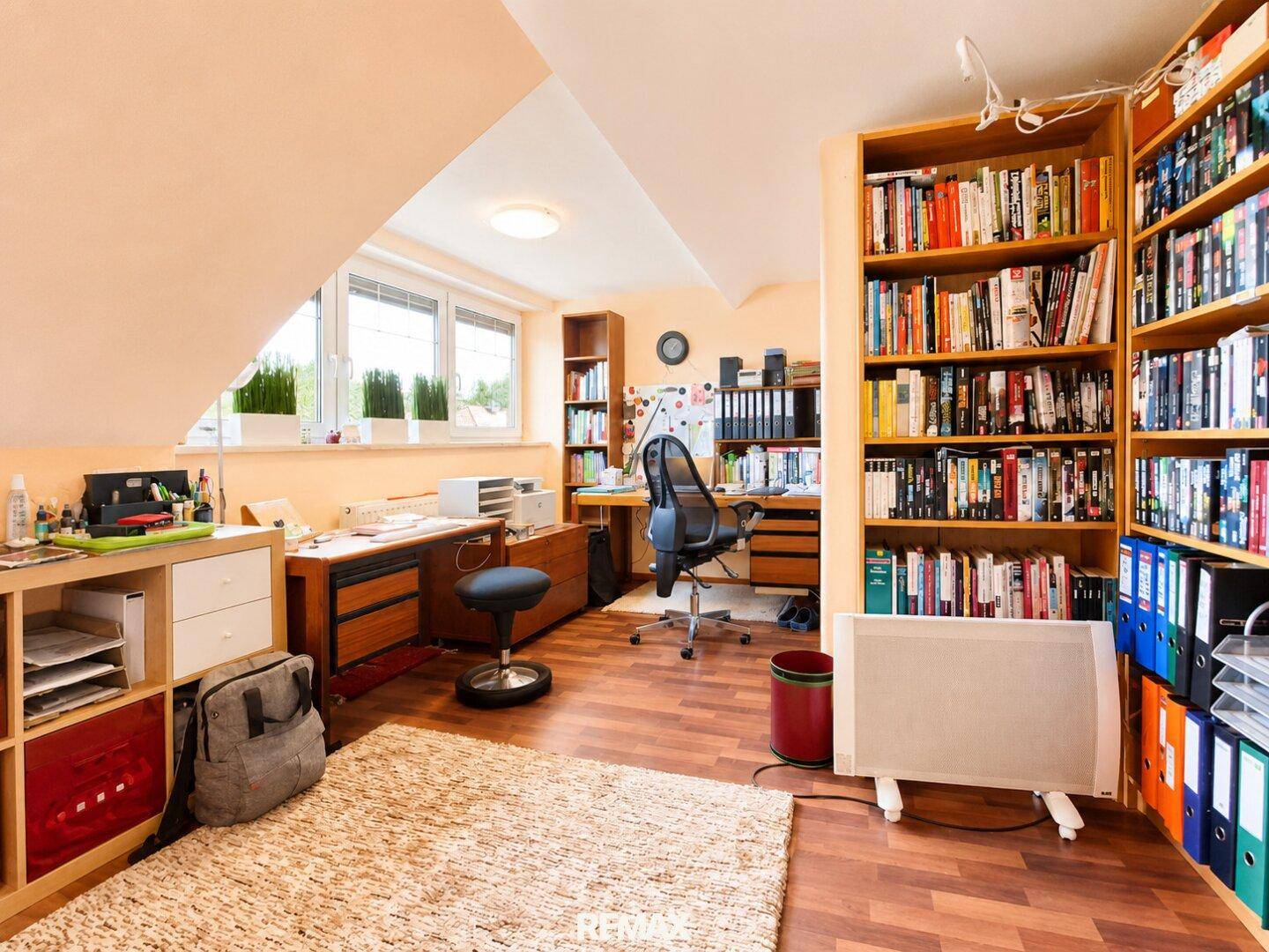 Helles Dachgeschoss-Büro mit Schreibtischen, Bücherregalen und Dachschrägen.