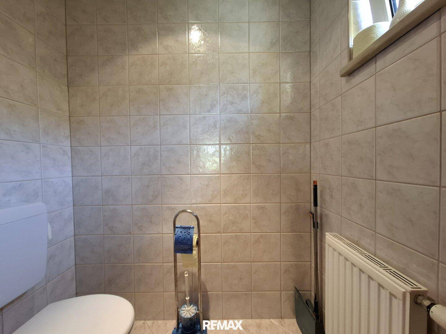 Kleines Gäste-WC mit hellen Fliesen an den Wänden und einem Fenster für Tageslicht.