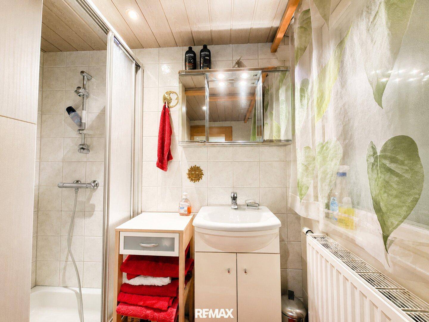 Funktionales Badezimmer mit Duschkabine, Waschbecken und Spiegelschrank, hell gefliest.