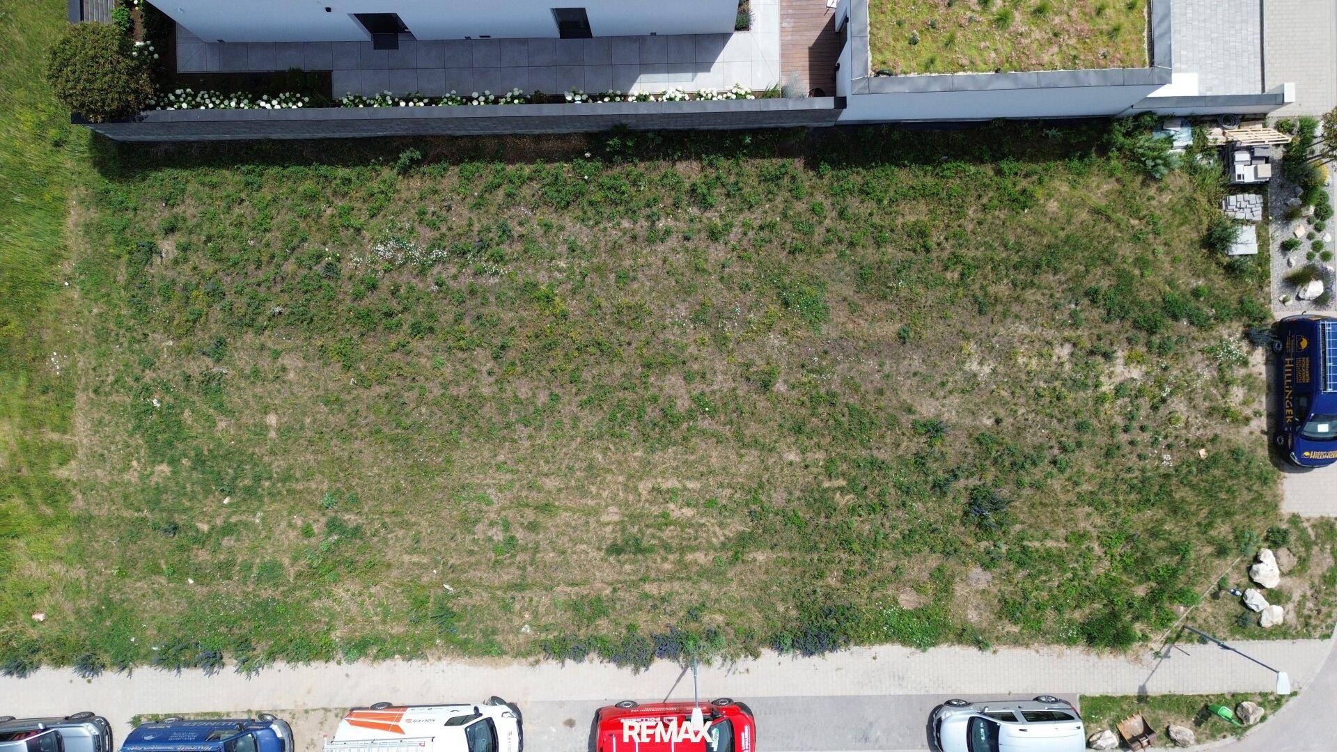 Luftaufnahme eines rechteckigen Grundstücks mit trockenem Gras, angrenzendem Wohnhaus und Straße.