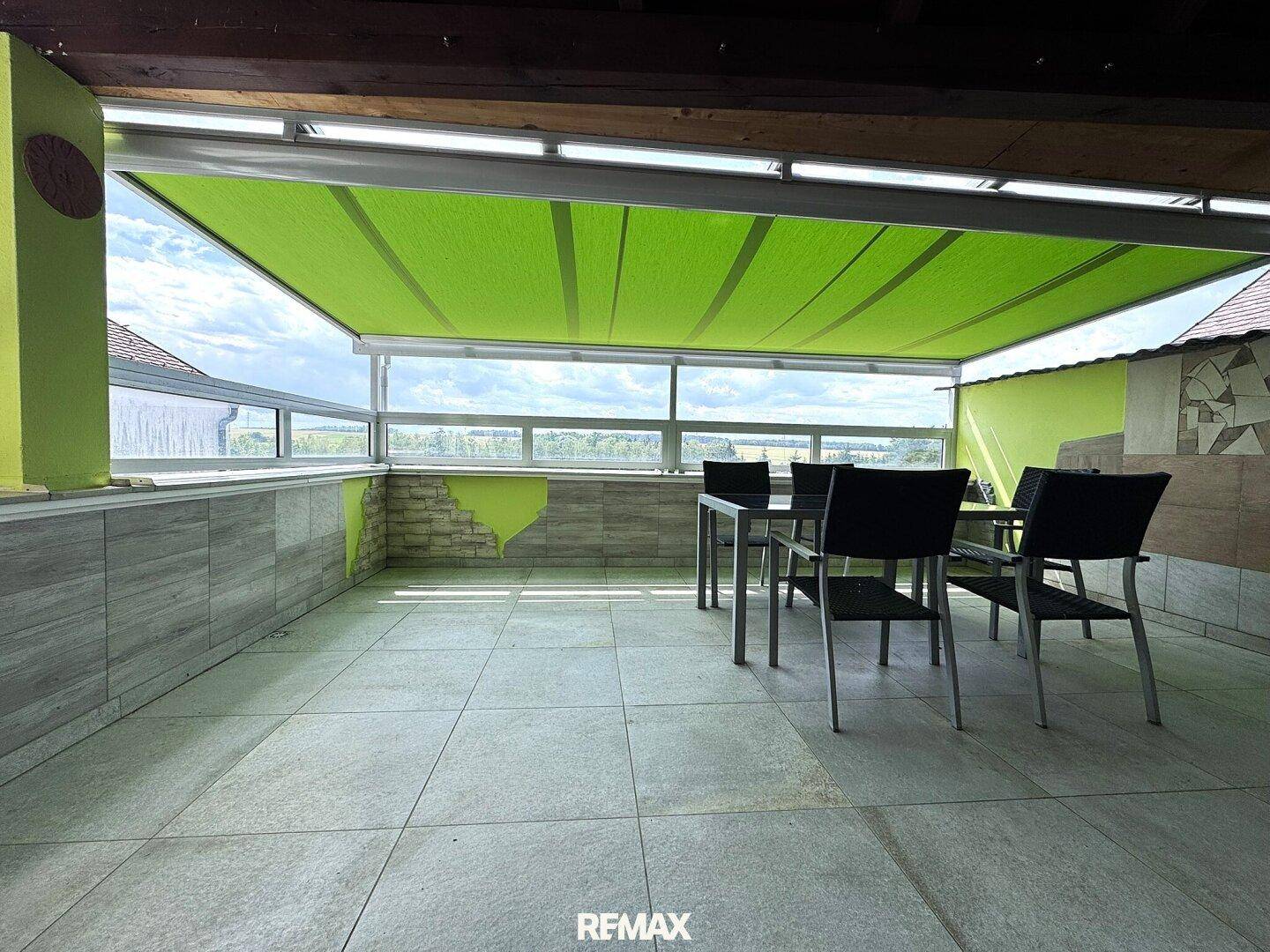 Überdachte Terrasse mit Fliesenboden und Sitzgelegenheiten, ideal für Mahlzeiten im Freien.