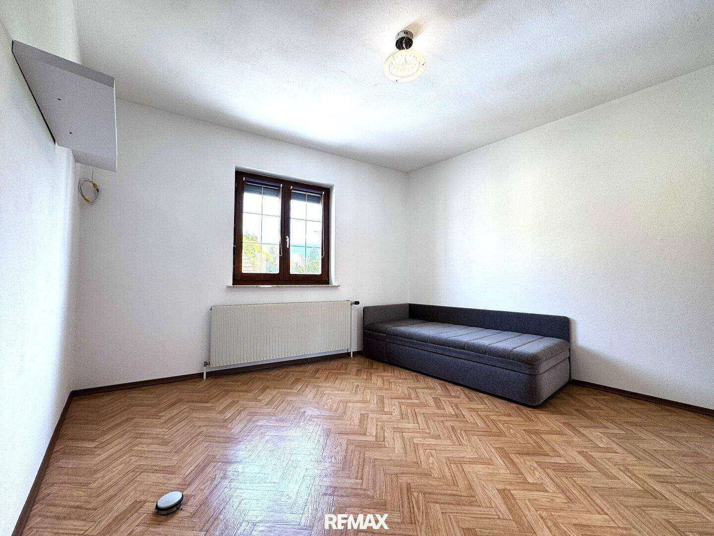 Helles Zimmer mit Fischgrätparkett und einem kleinen Sofa, vielseitig nutzbar.