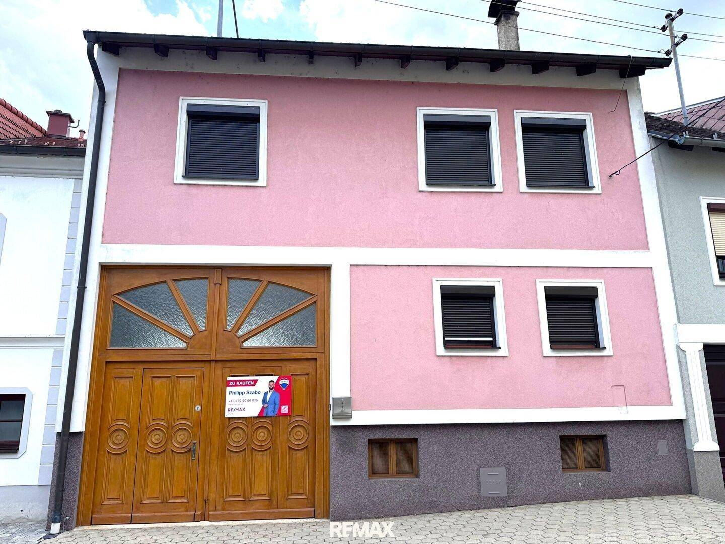 Rosa Hausfassade mit dunklen Rollläden und einem großen hölzernen Garagentor.