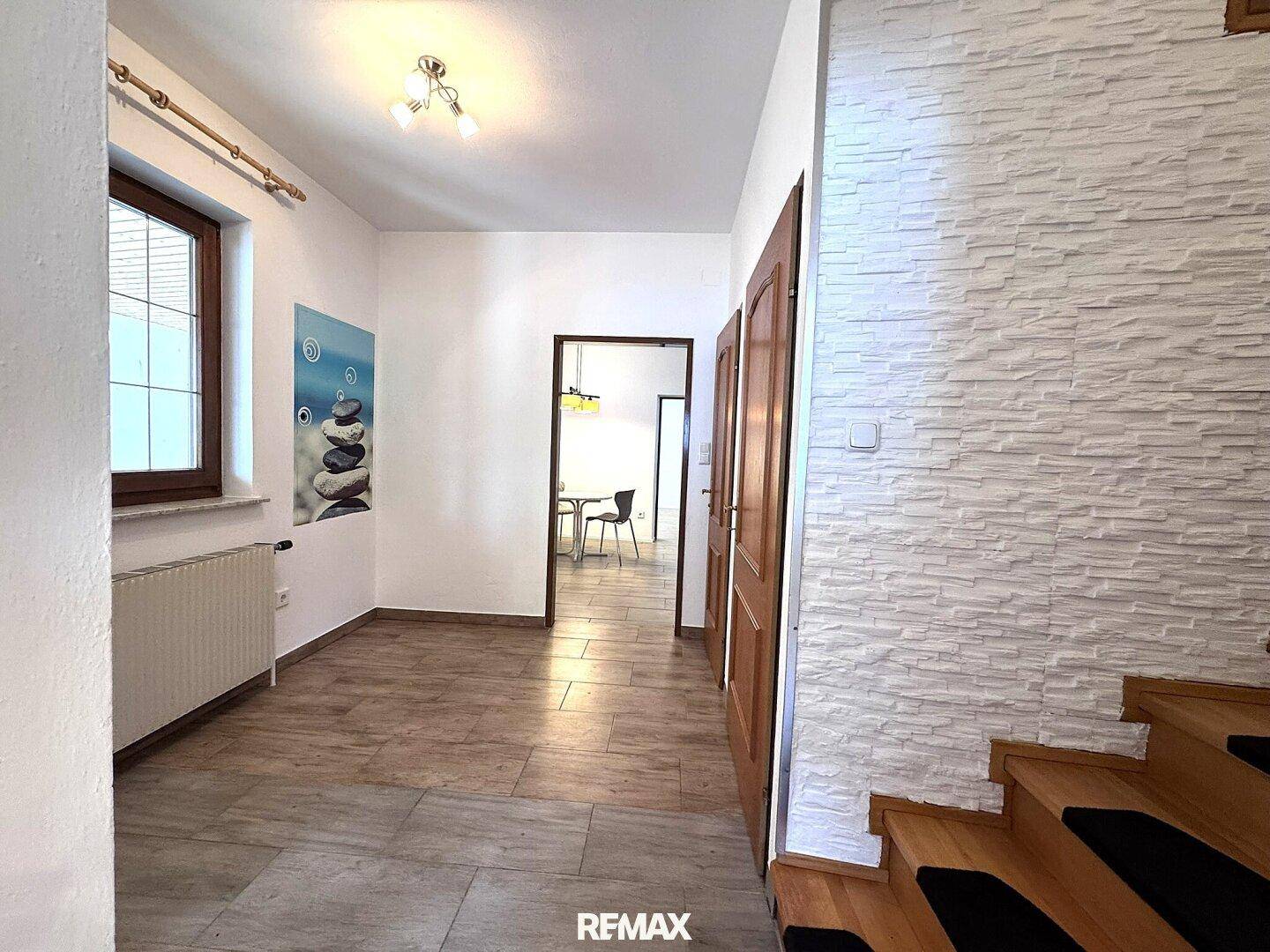 Heller Flur mit Fliesenboden, strukturierter Wand und Holztreppe.
