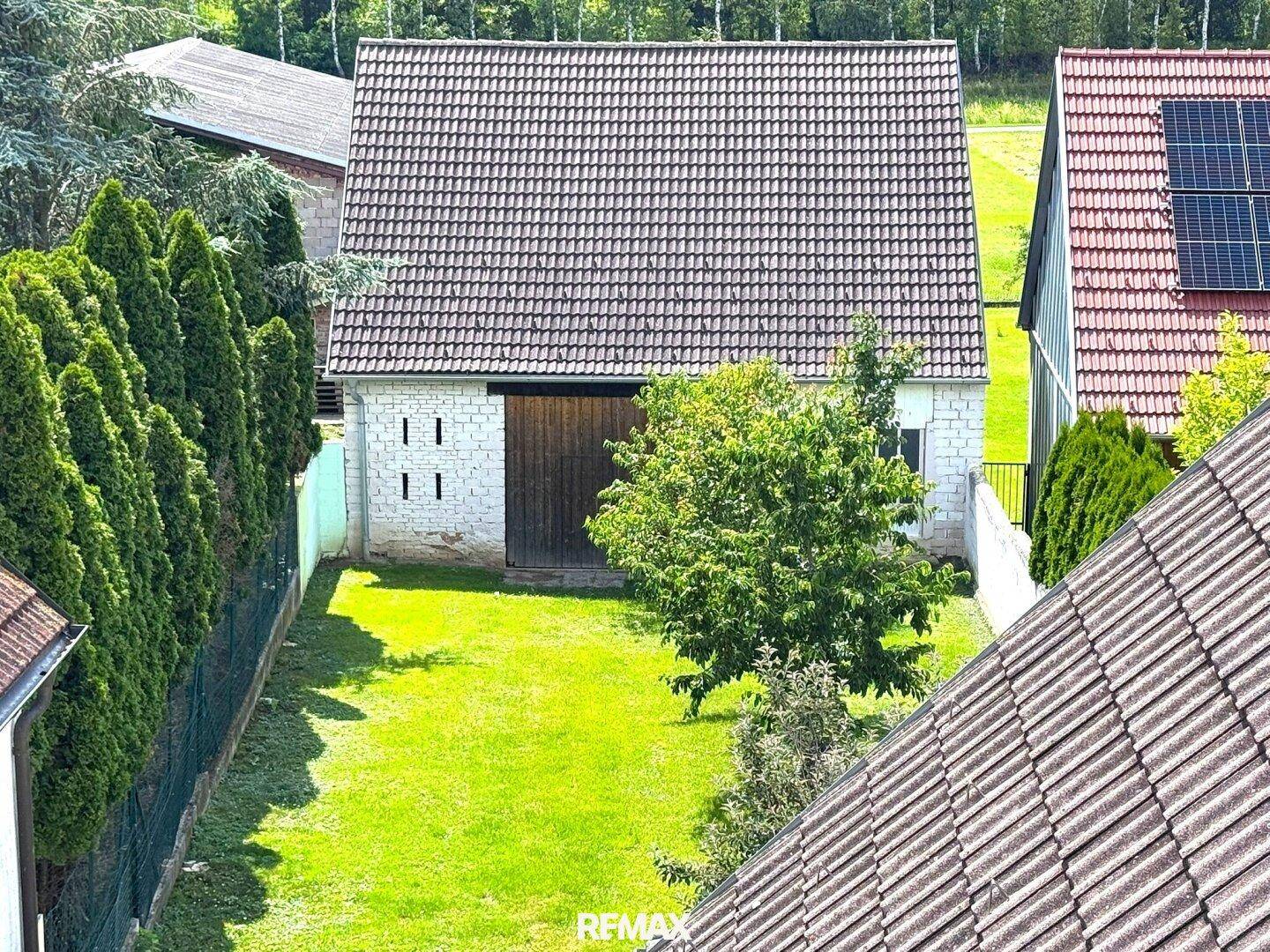 Luftaufnahme eines Gartens mit Rasen, Bäumen und einem Gebäude mit Solaranlage.