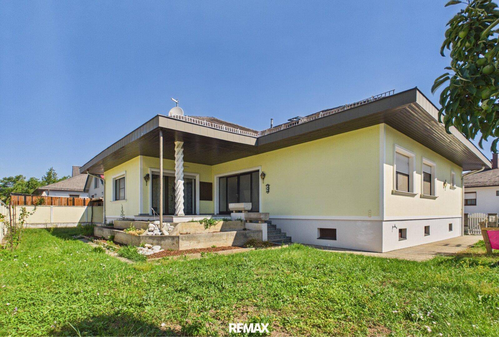 Rückseite des Hauses mit überdachter Terrasse, Säulen und einem gepflegten Rasenbereich.