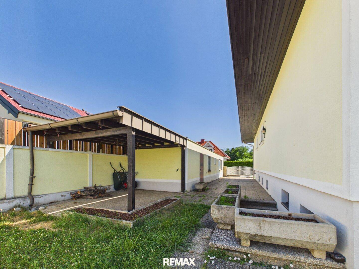 Seitenansicht des Hauses mit einem Carport, Gartenbereich und Betonkübeln.