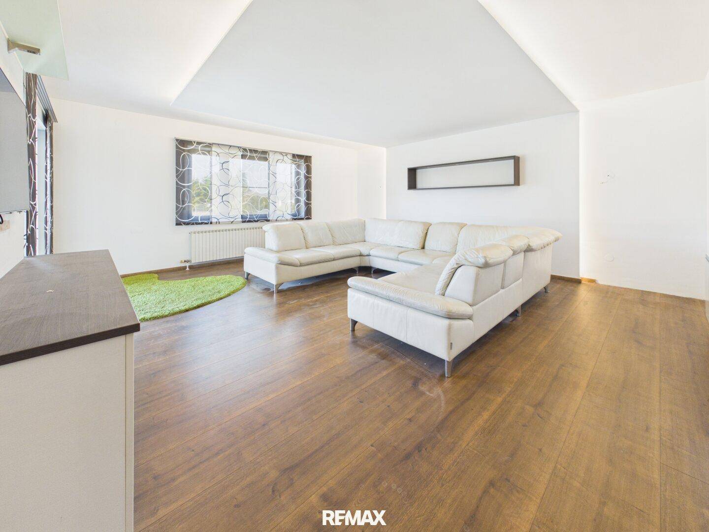 Gemütliches Wohnzimmer mit Holzboden, Ecksofa und moderner Deckengestaltung.