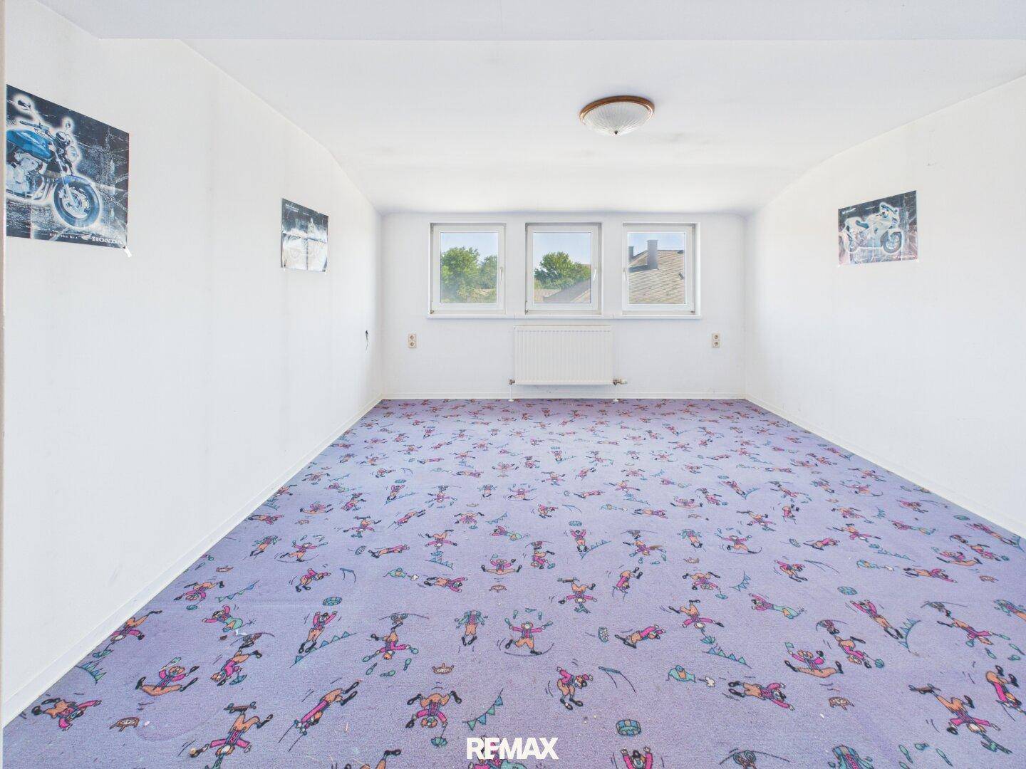 Helles Zimmer mit auffälligem Teppichboden und drei Fenstern für viel Licht.