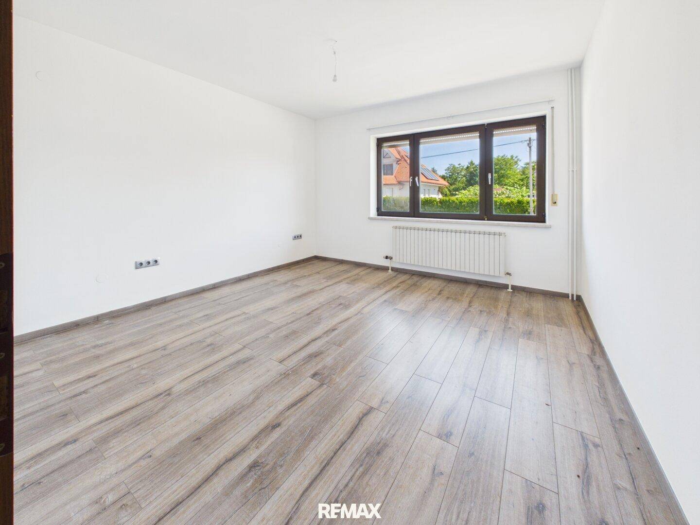 Geräumiges, leeres Zimmer mit modernem Laminatboden und großem Fenster.
