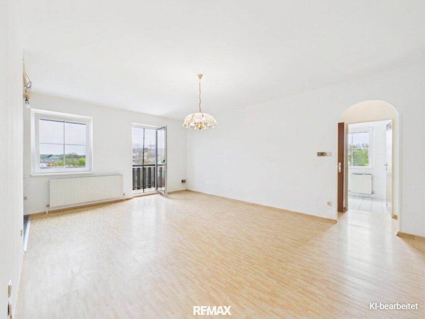 Helles, leeres Wohnzimmer mit Laminatboden und Zugang zu einem französischen Balkon.
