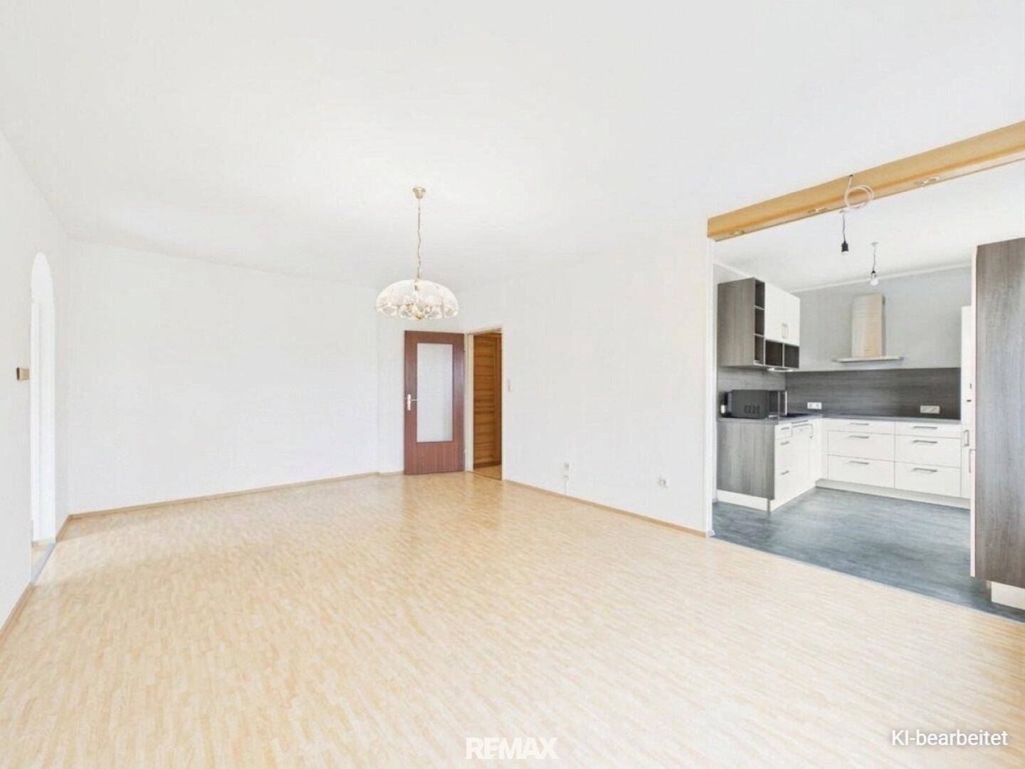 Geräumiges Wohnzimmer mit Laminatboden und offenem Übergang zu einer modernen Küche.