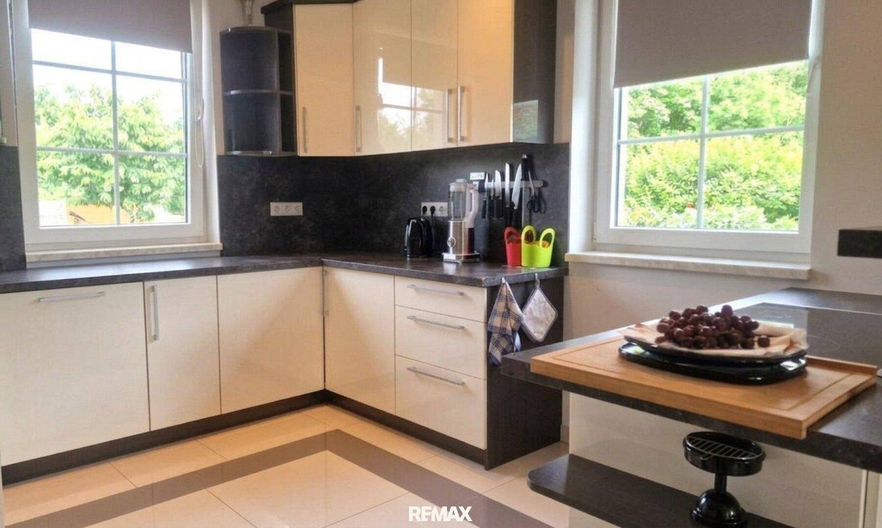Moderne Küche mit glänzenden cremefarbenen Schränken und dunkler Arbeitsplatte.