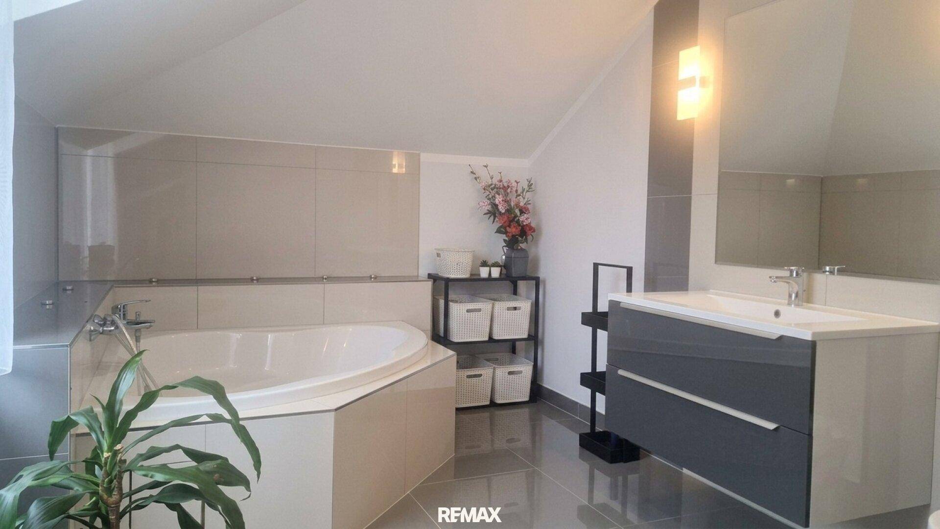 Geräumiges Badezimmer mit Eckbadewanne, modernem Waschtisch und grauen Fliesen.