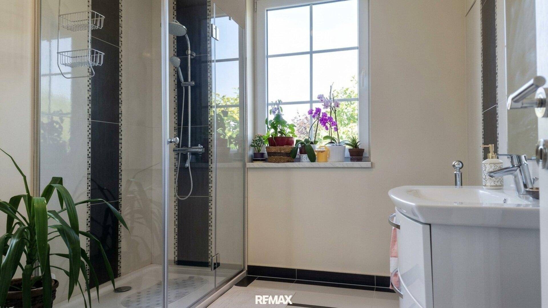 Modernes Badezimmer mit Duschkabine, Fenster und Pflanzen auf der Fensterbank.