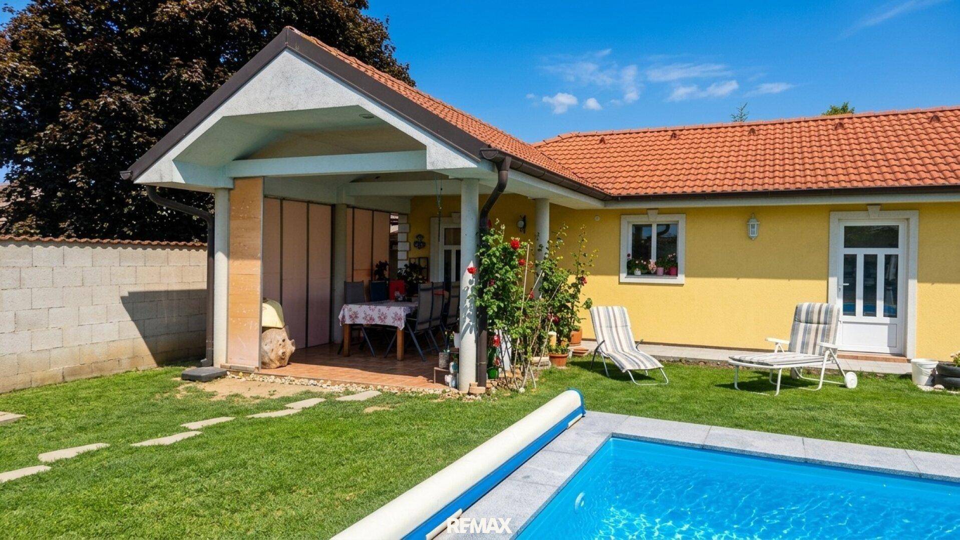 Überdachte Terrasse mit Sitzgelegenheiten, Blick auf den Pool und Garten.