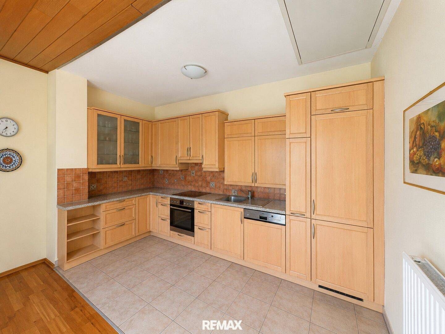 Funktionale Küche mit Holzfronten, Fliesenboden und integrierten Geräten.