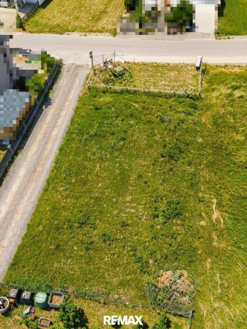 Draufsicht auf ein weitläufiges, unbebautes Grundstück mit Grasfläche und angrenzenden Wegen.