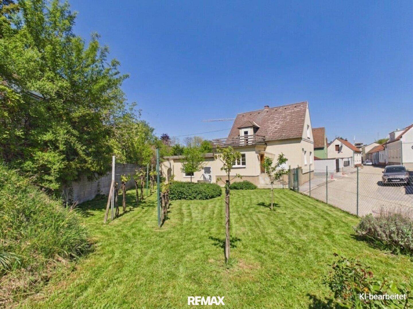Großer Garten mit Rasenfläche und jungen Bäumen, der zum Haus hinaufführt.