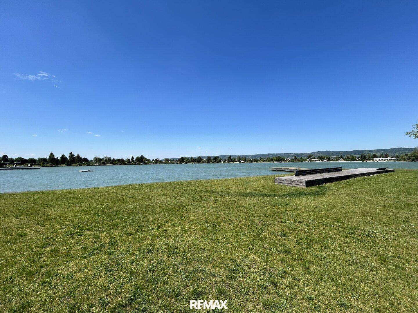 Panoramablick auf den See mit einer großen Rasenfläche und Holzplattformen am Ufer.