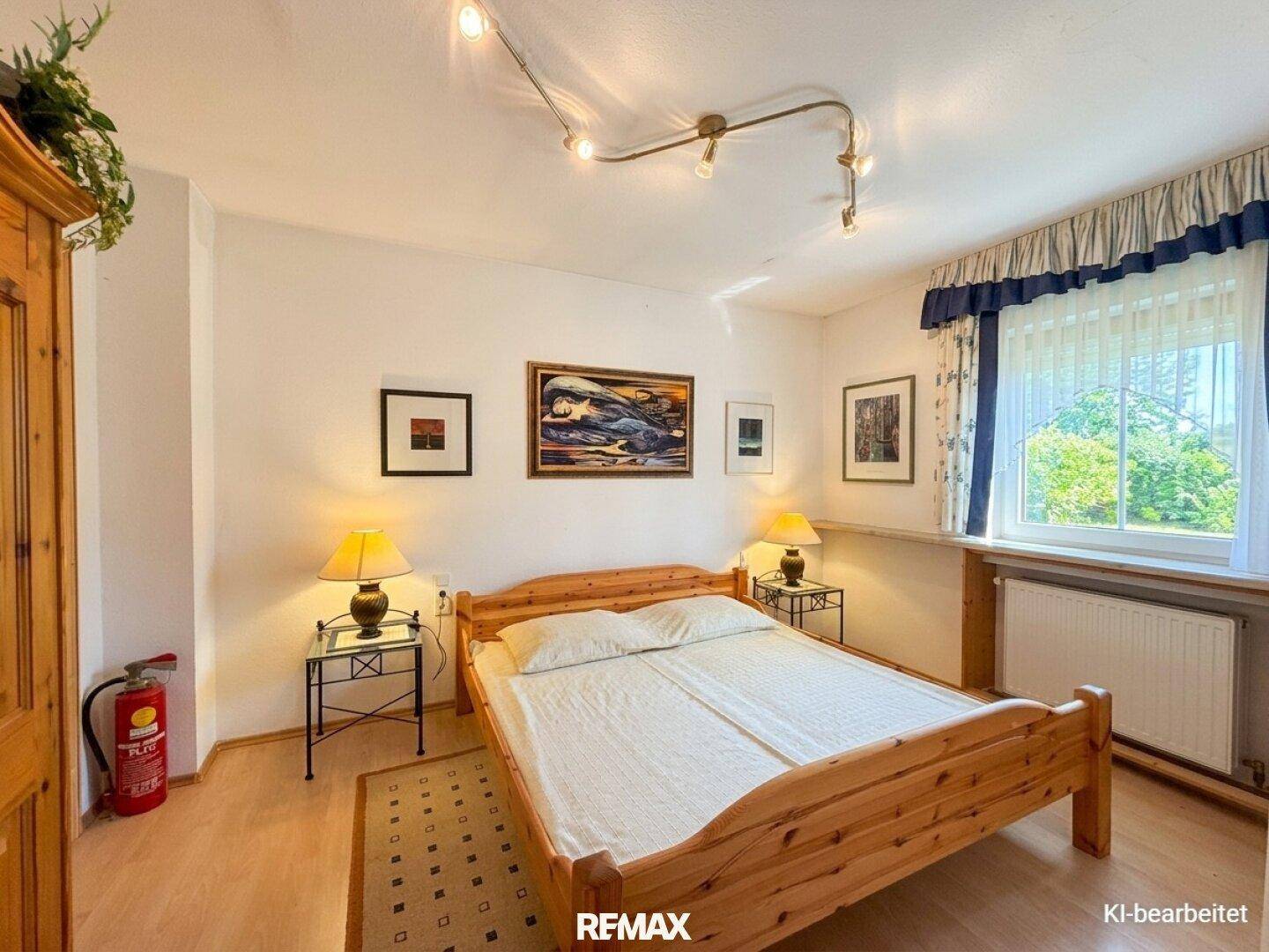 Helles Schlafzimmer mit Holzbett, Laminatboden und Fenster mit Blick ins Grüne.