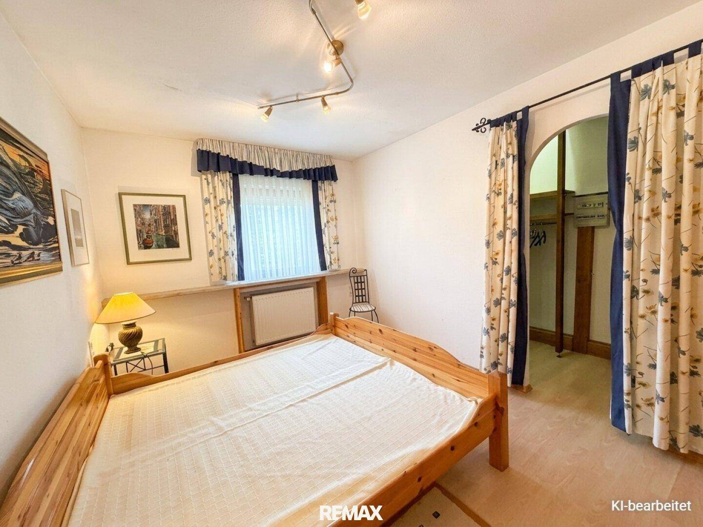 Schlafzimmer mit Holzbett, Laminatboden und einem offenen Durchgang zu einem Ankleidebereich.