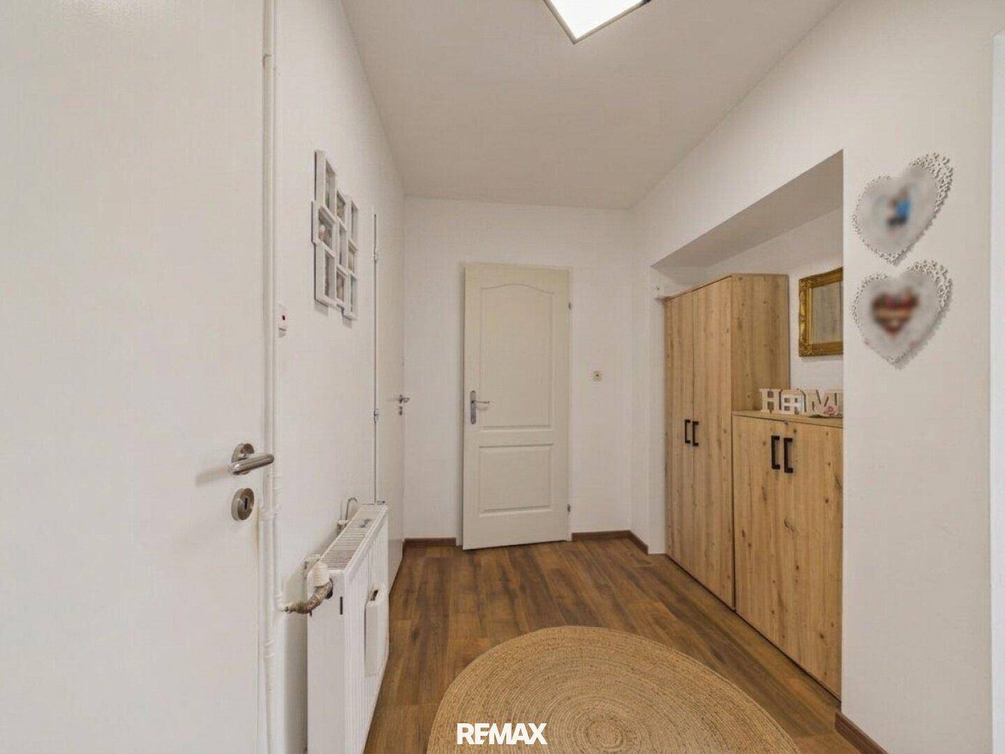 Heller Flur mit Holzboden und weiß gestrichenen Wänden, ausgestattet mit einem Holzschrank.