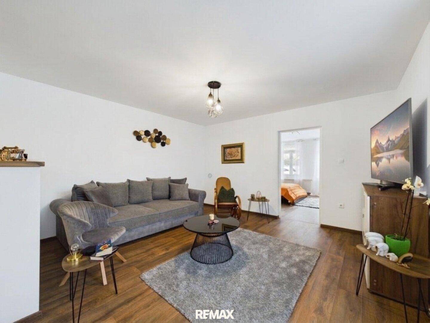 Gemütliches Wohnzimmer mit grauem Sofa, modernem Couchtisch und Holzboden, mit Zugang zu einem weiteren Raum.