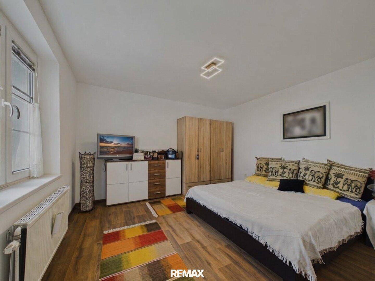 Schlafzimmer mit Holzboden, großem Kleiderschrank und einem Bett, dekoriert mit einem farbenfrohen Teppich.